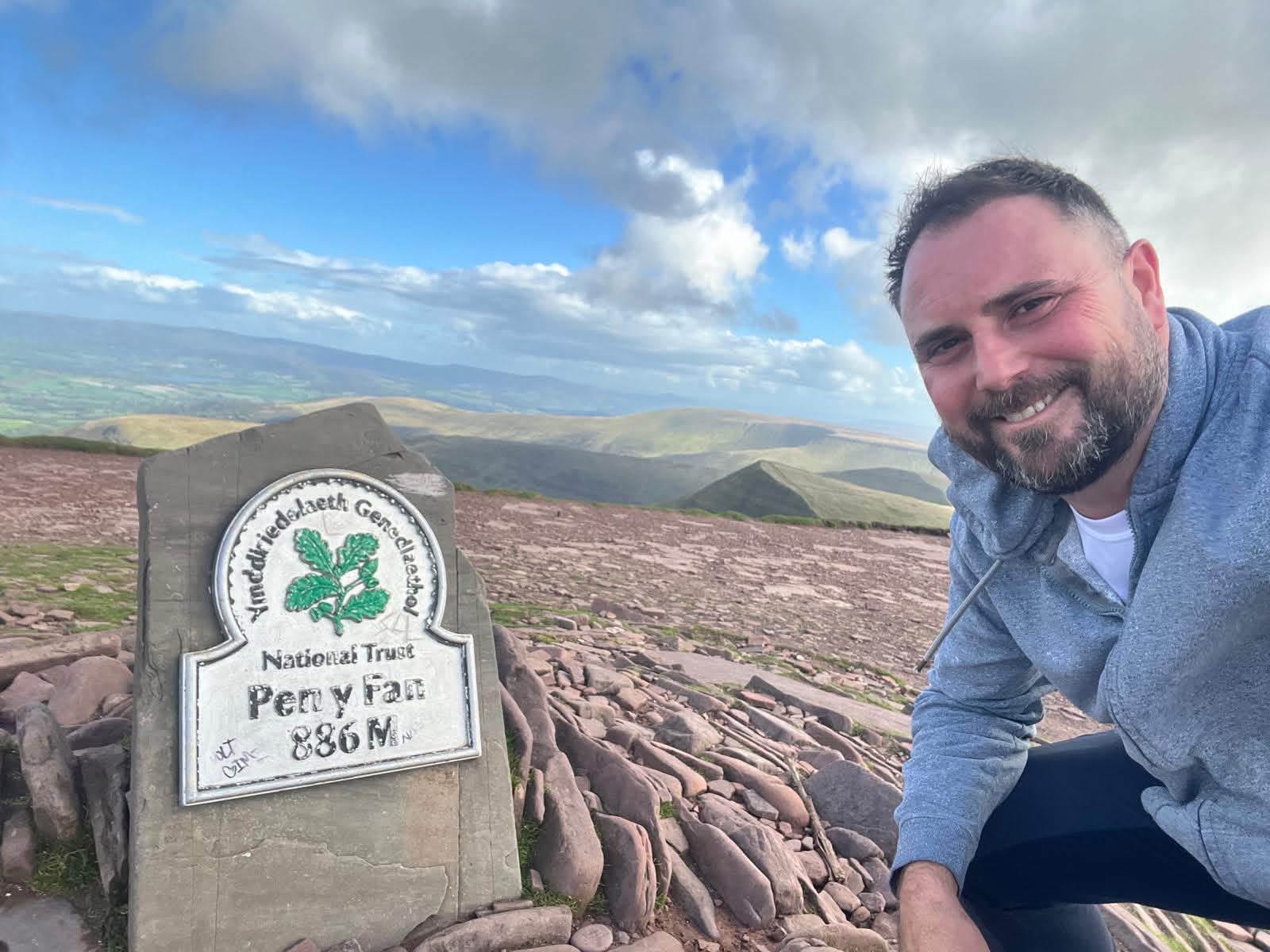 A member crouched beside the Pen y Fan summit marker