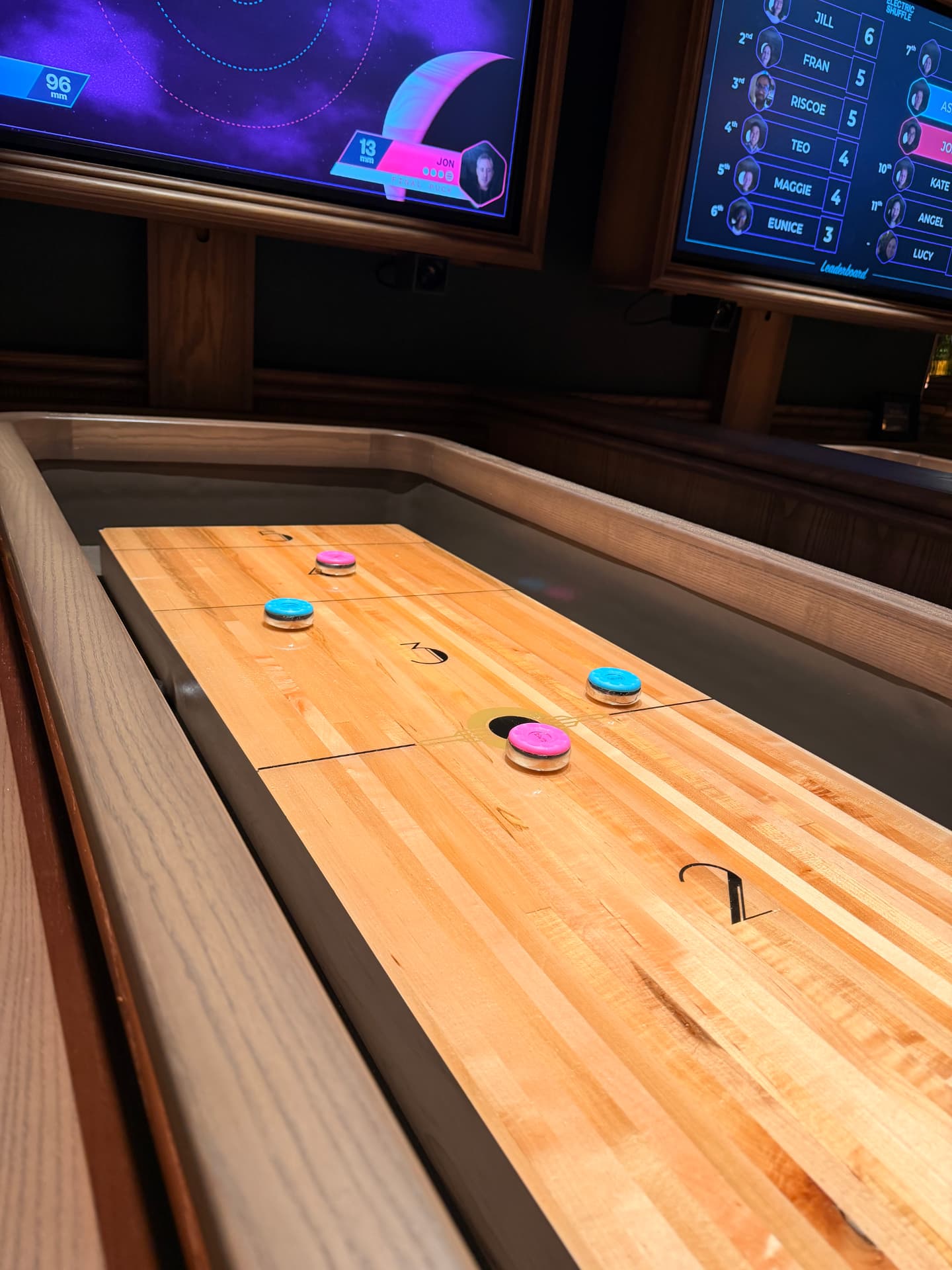 A shuffleboard table mid-game, pucks resting on the scored lanes