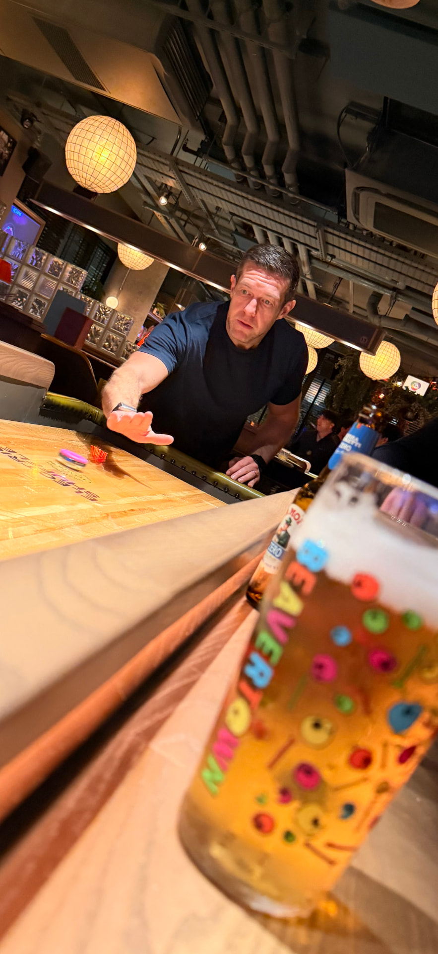 A member leaning in to play shuffleboard, a pint sitting on the table in front